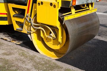 Yellow steamroller compacting fresh asphalt on a road.