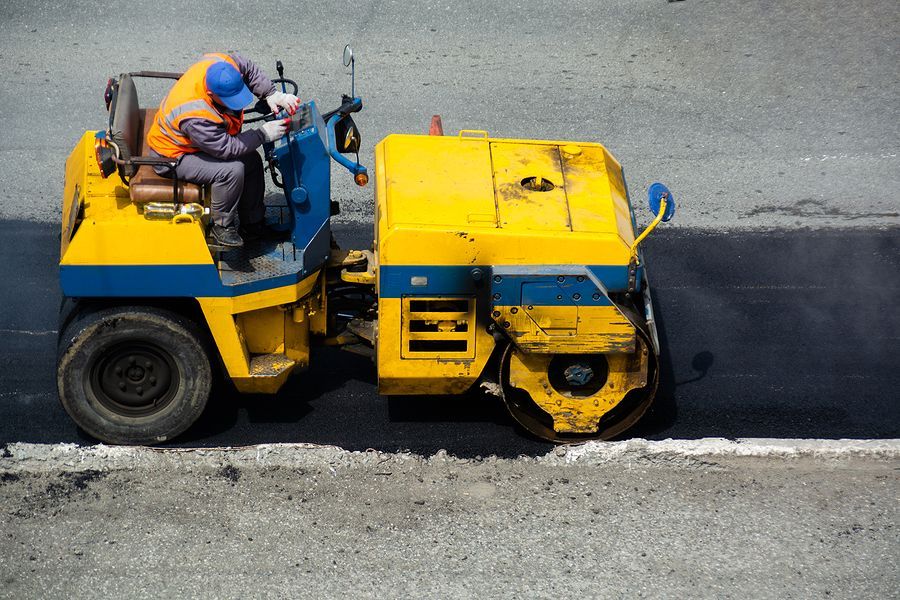Construction worker operating yellow and blue asphalt roller.