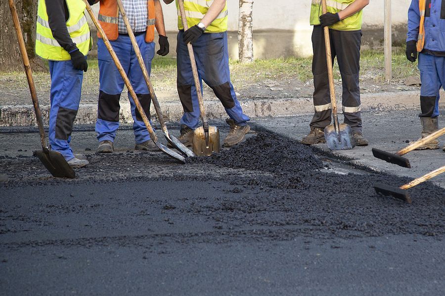 Construction workers leveling asphalt with shovels, wearing safety vests and work boots outdoors.