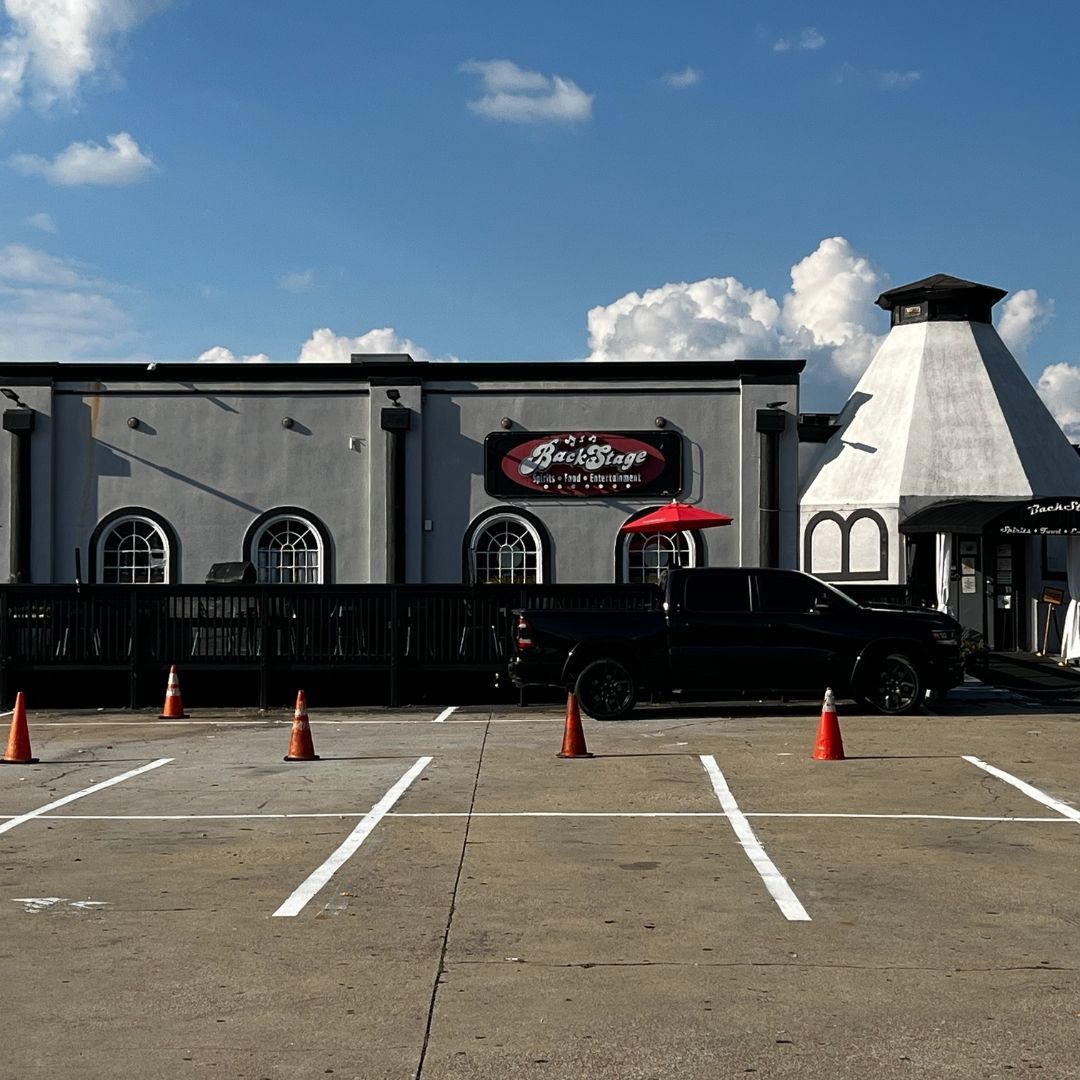 Exterior of a gray building with a black fence and parking spaces. A black pickup truck parks in front.
