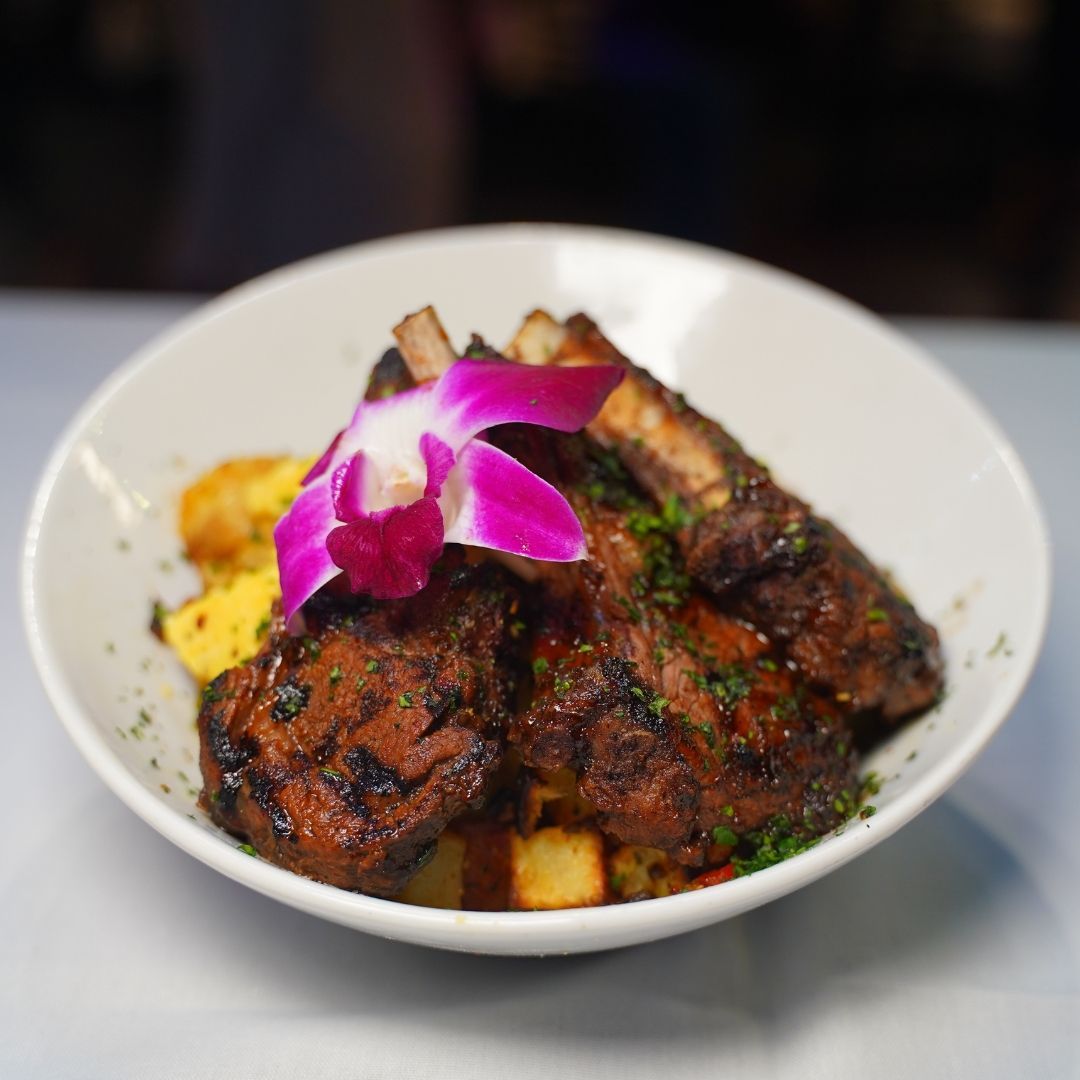 Grilled pork ribs with potatoes, garnished with an orchid, in a white bowl.