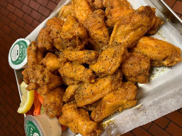 A platter of golden-brown, seasoned chicken wings with ranch dipping sauce, lemon wedges, and carrot sticks.