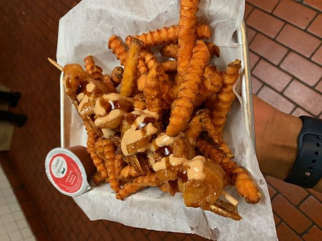 Sweet potato fries and corn dogs on a tray with a sauce drizzle and a dipping sauce.