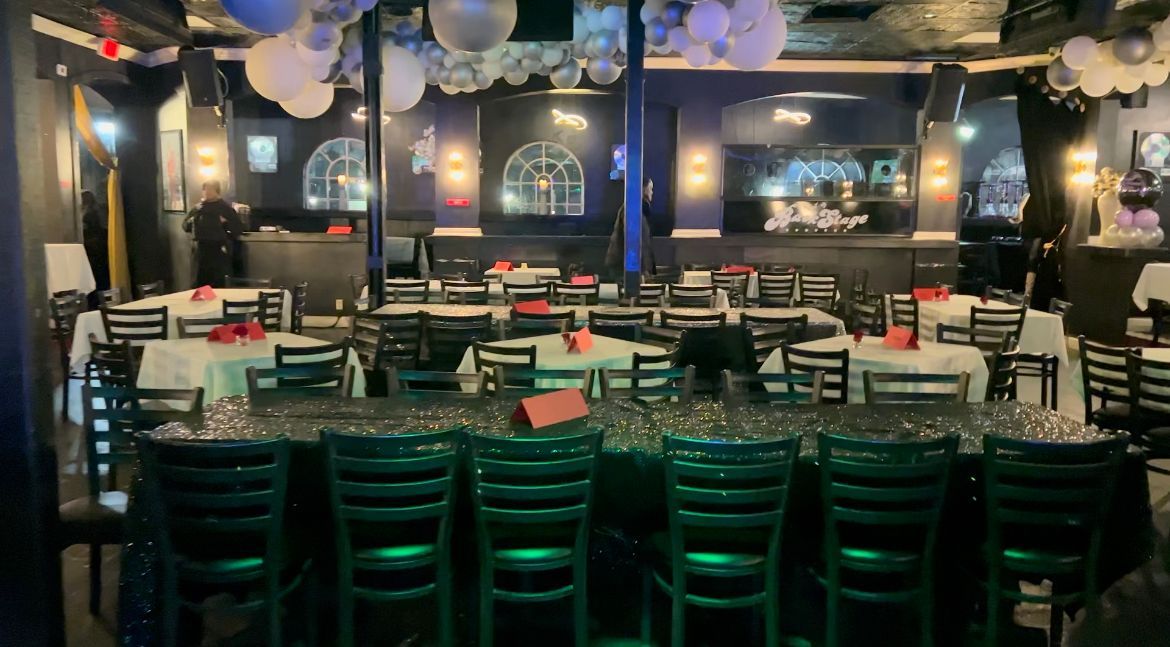 A brightly lit bar and restaurant with tables set for a gathering. White and silver balloons hang from the ceiling.