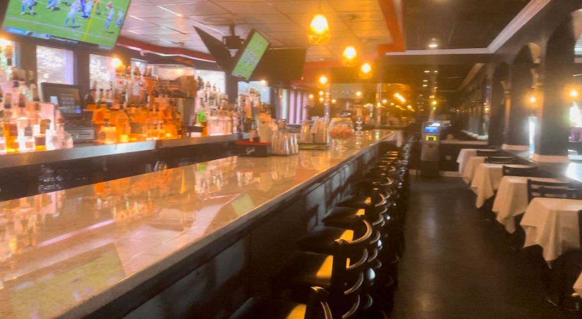 A long bar in a dimly lit restaurant. Empty barstools line the counter.