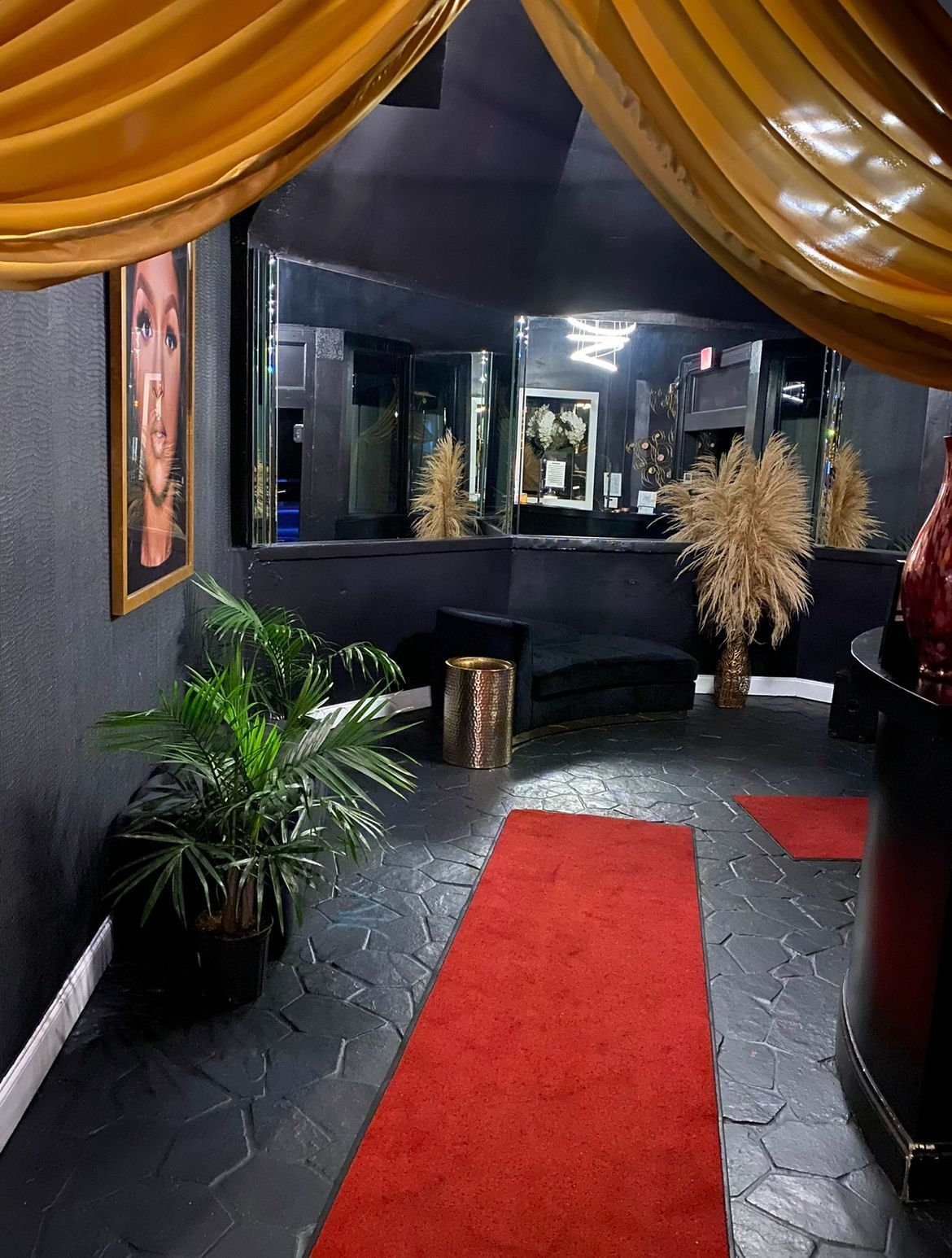 Dark-themed room with red carpet, plants, gold accents, and mirrors. A golden curtain drapes from the ceiling.