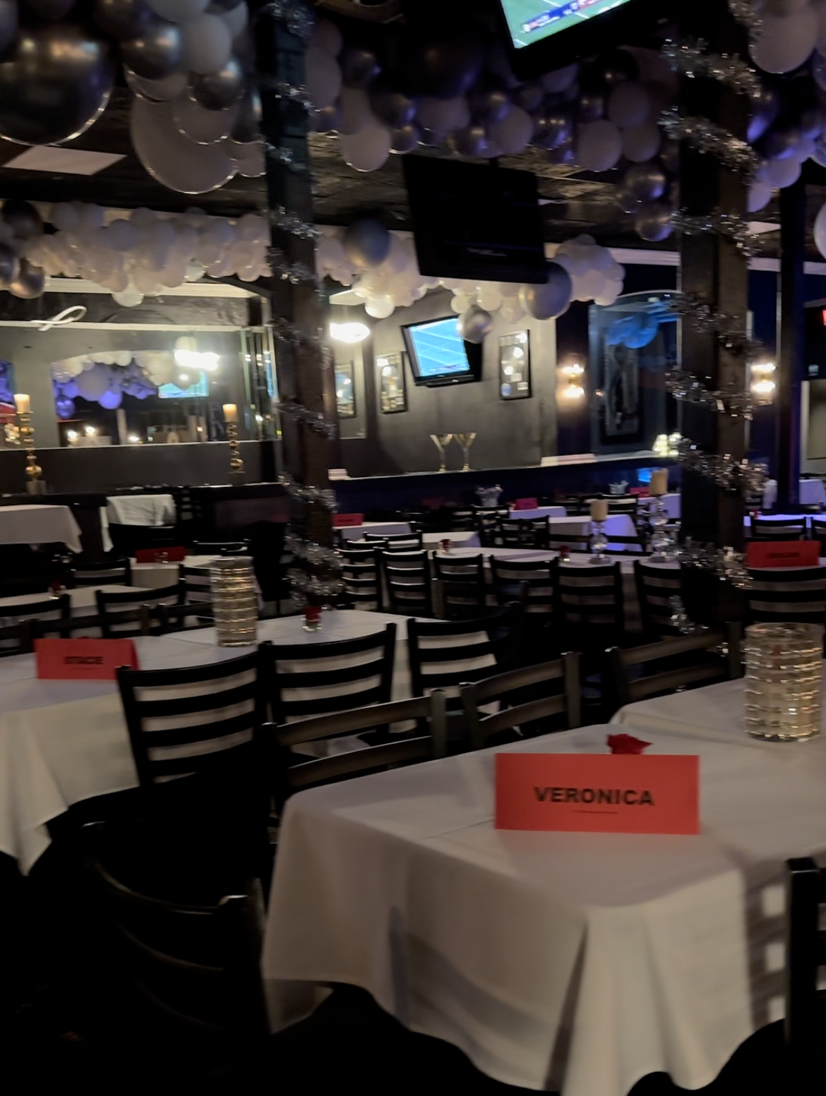 Indoor restaurant decorated with white balloons, tables set for guests. Red place cards read 