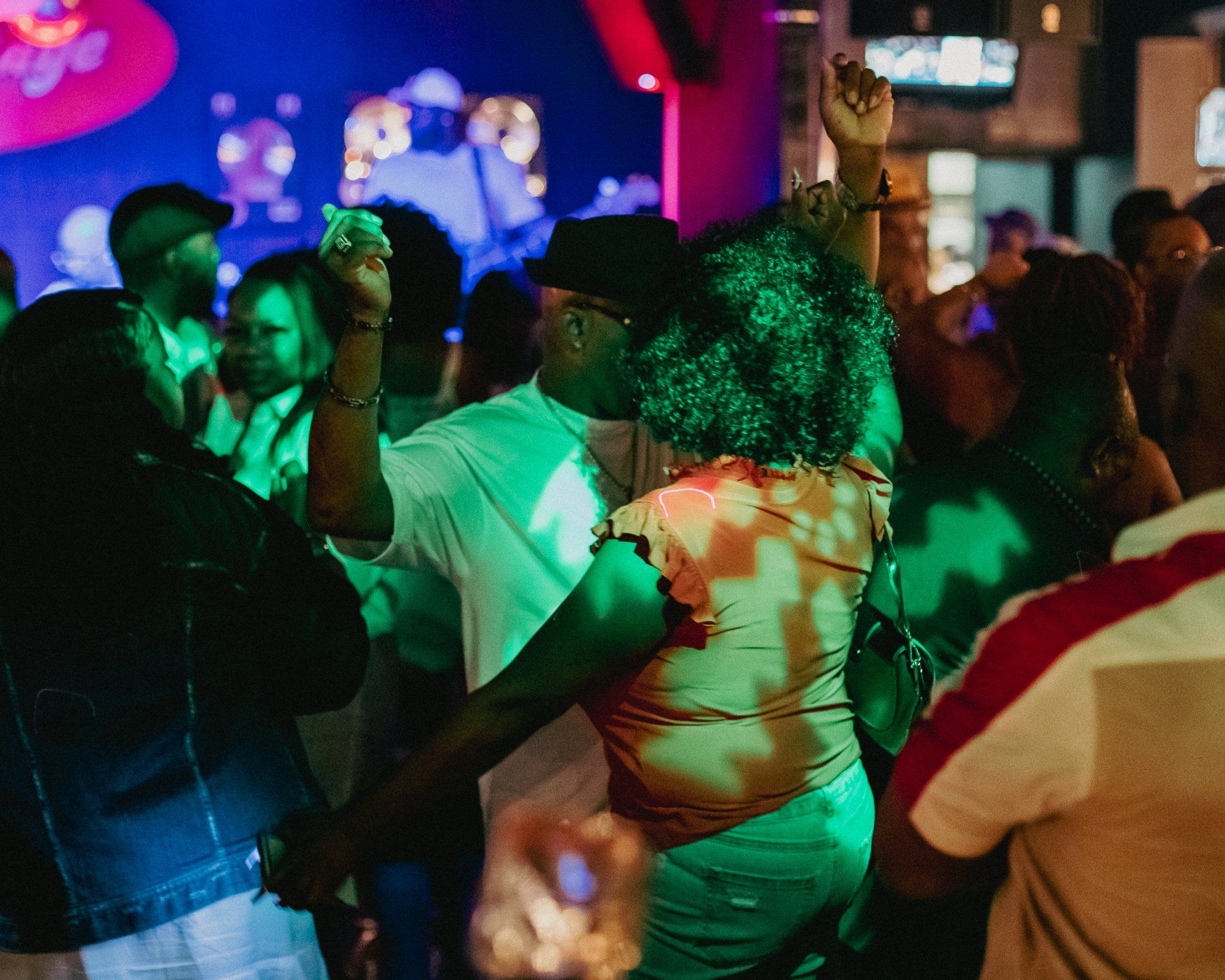 People dancing at a nighttime event with colorful lights. A couple dances in the center, arms raised.