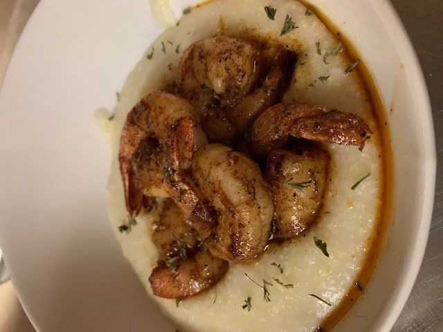 Shrimp and grits, a dish with seasoned shrimp atop creamy white grits, garnished with parsley, in a white bowl.