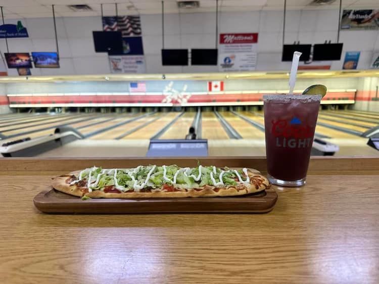 A bowling alley with a pizza and a drink on a table