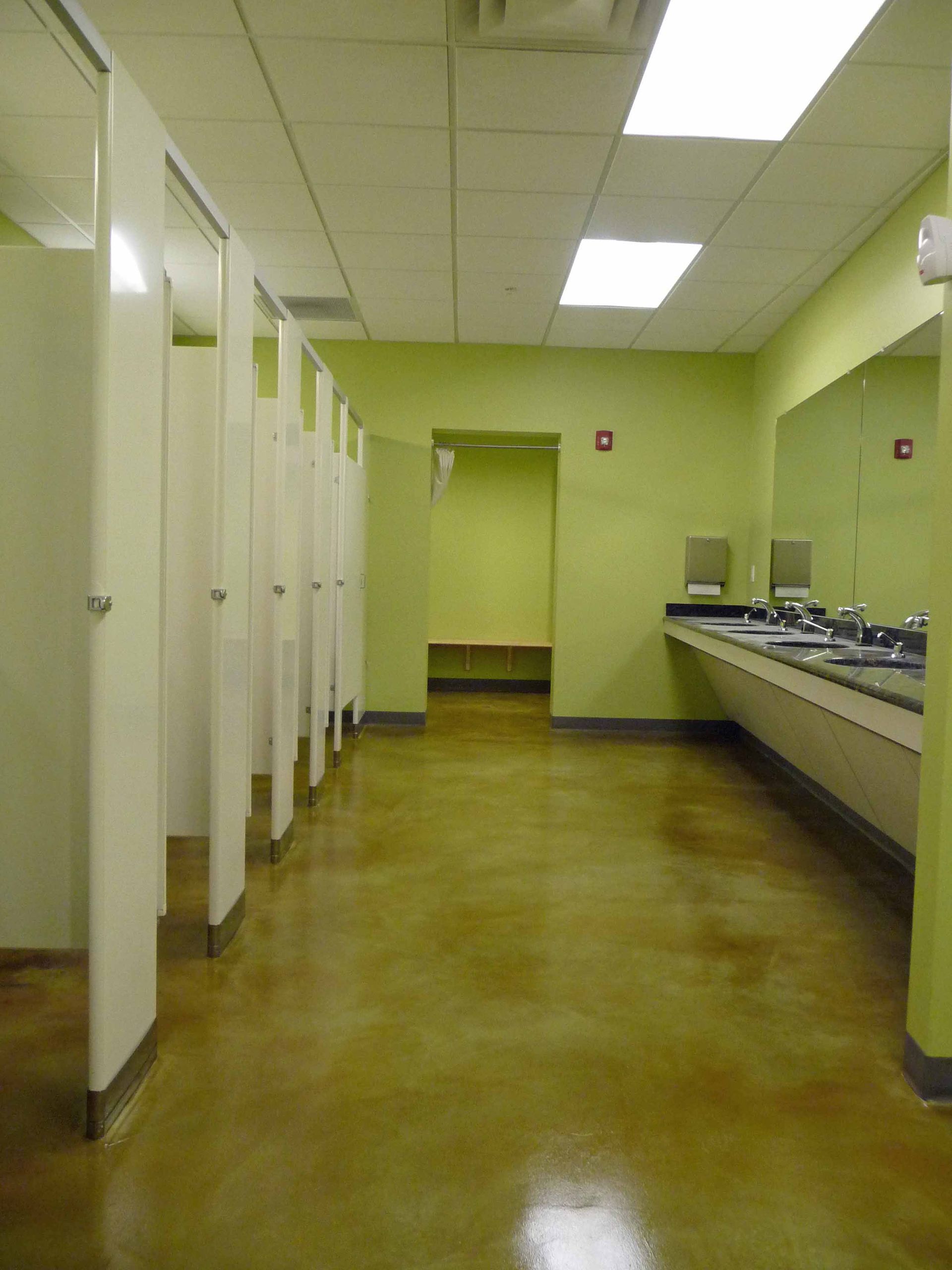 Public restroom with stalls, sinks, and a light green wall. Brown floor.