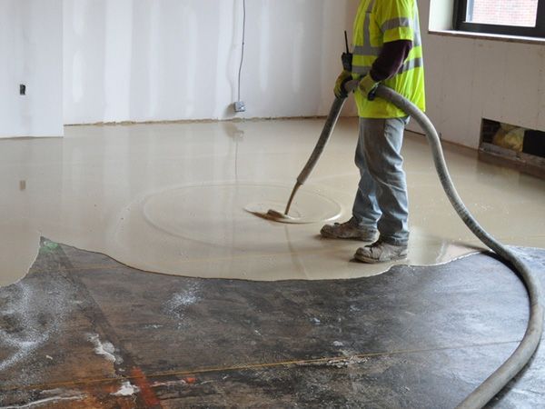 Worker smoothing wet flooring compound with a trowel in a construction site.