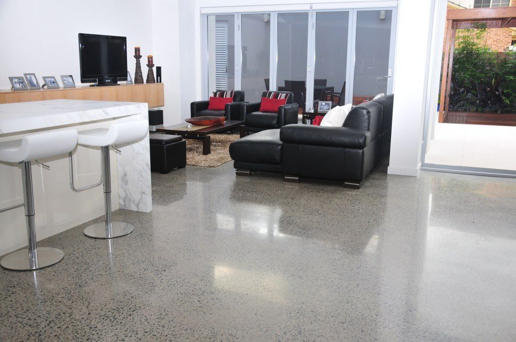 Polished concrete floor in a modern living room with black leather sofa and white bar stools.
