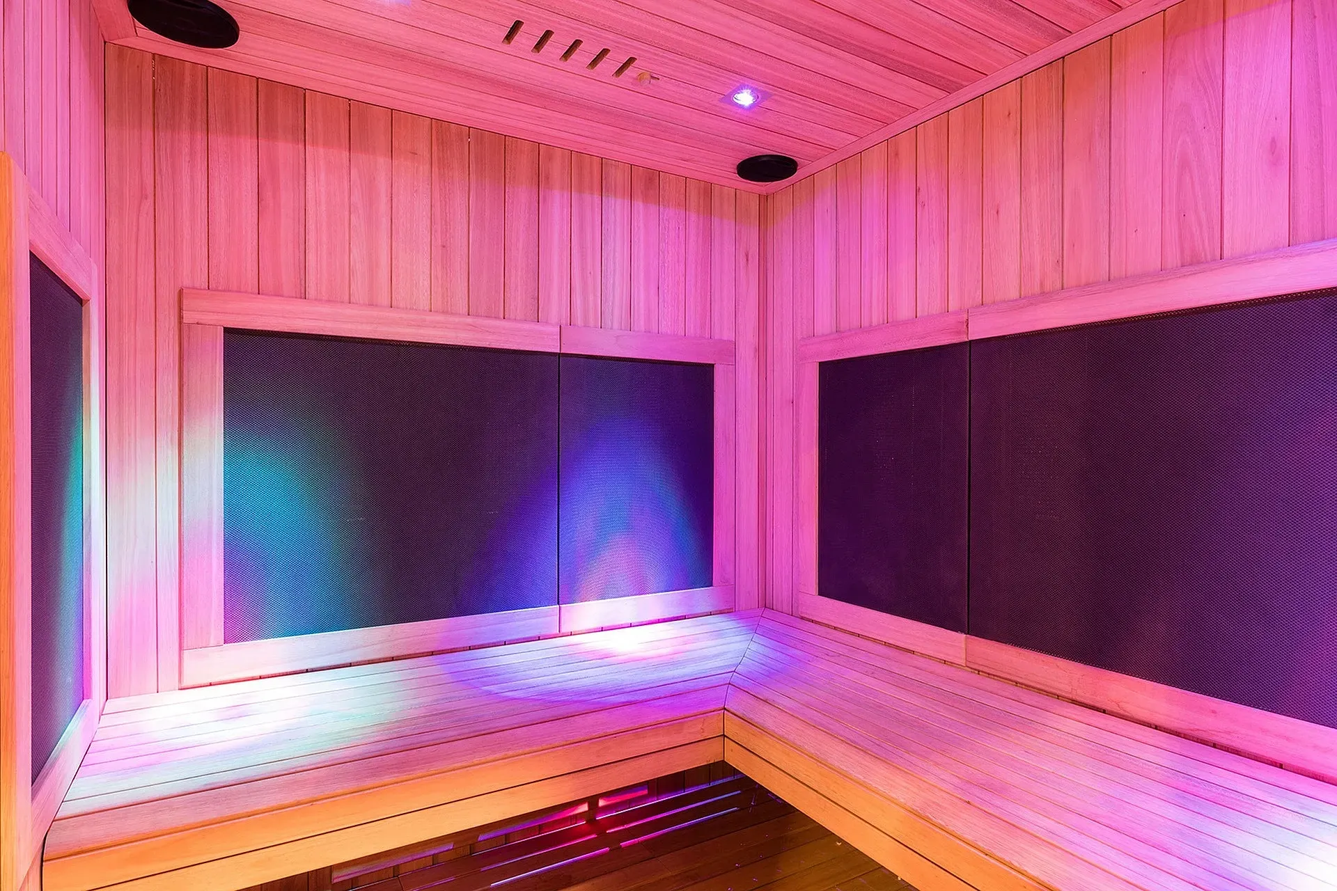 Wood paneled sauna interior with two-tier benches and purple-pink lighting.