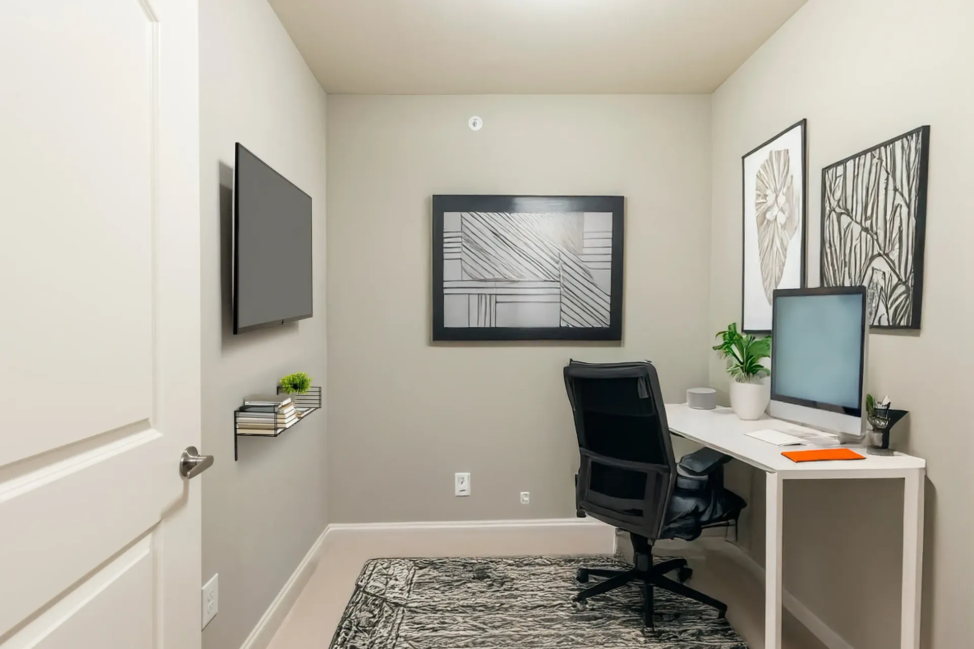 Small home office setup with white desk, black chair, large monitor, and framed wall art.