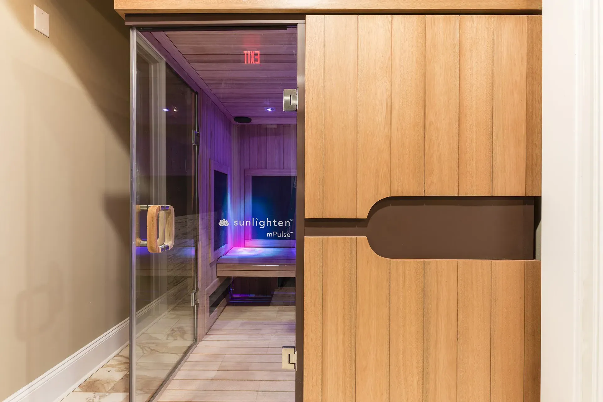 Glass door entry to a wood-paneled community sauna with purple lighting.