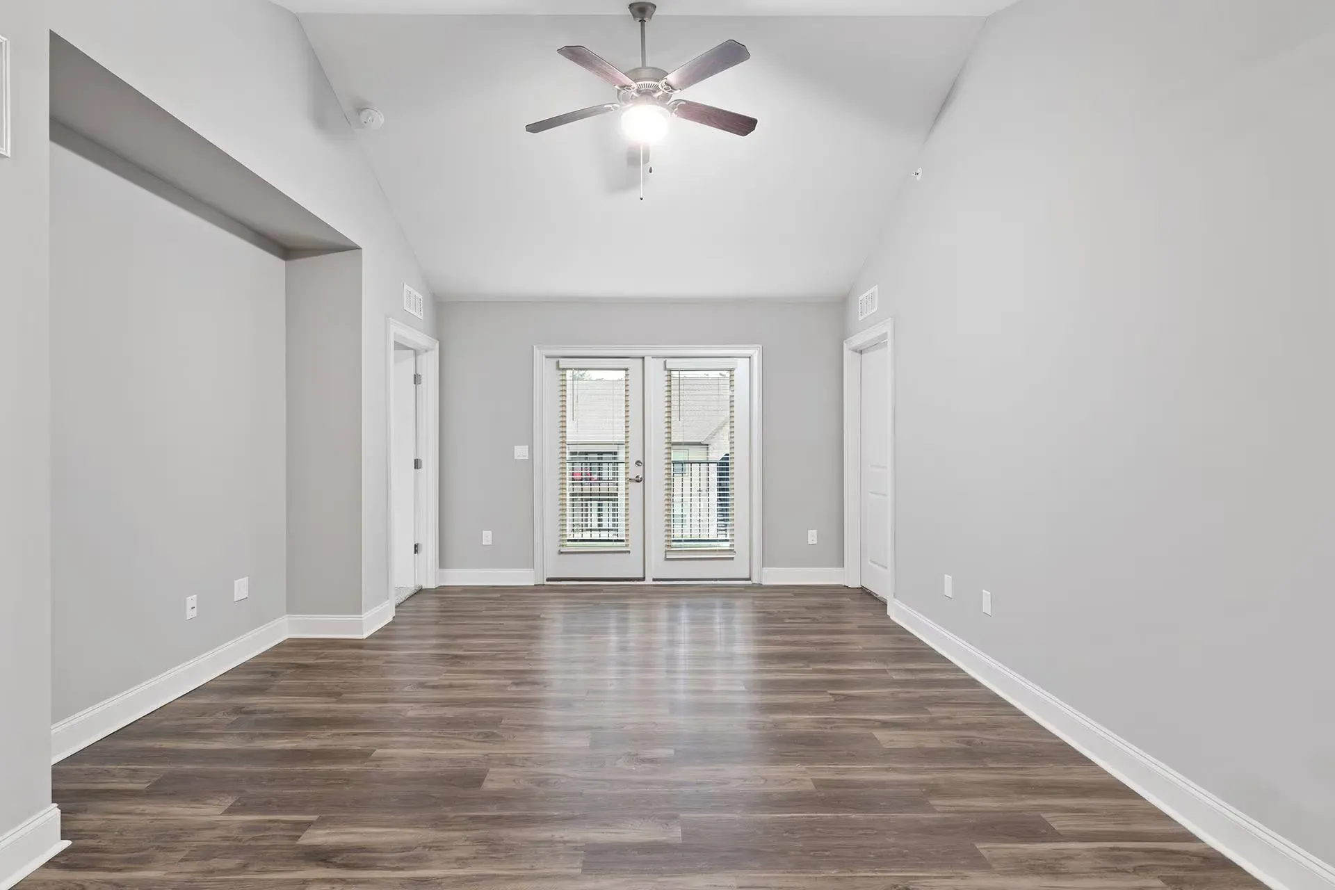 Empty living room with gray walls, wood-like flooring, and French doors.