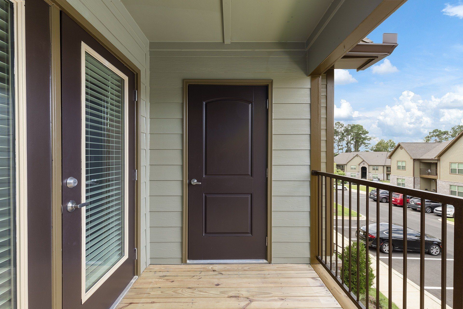 Balcony view of a multifamily building with a dark brown door and railing overlooking a parking lot.