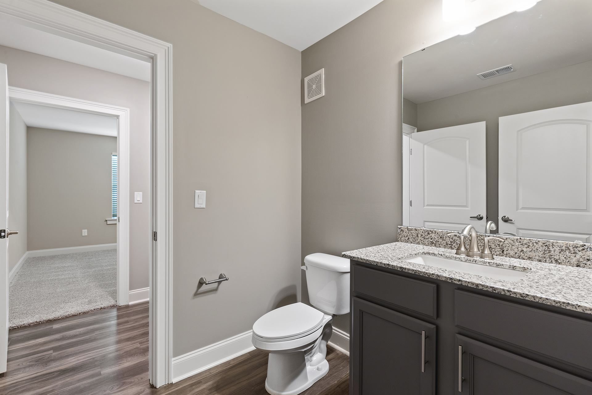 Bathroom with granite vanity, sink, mirror, toilet, and doorway to a carpeted room.