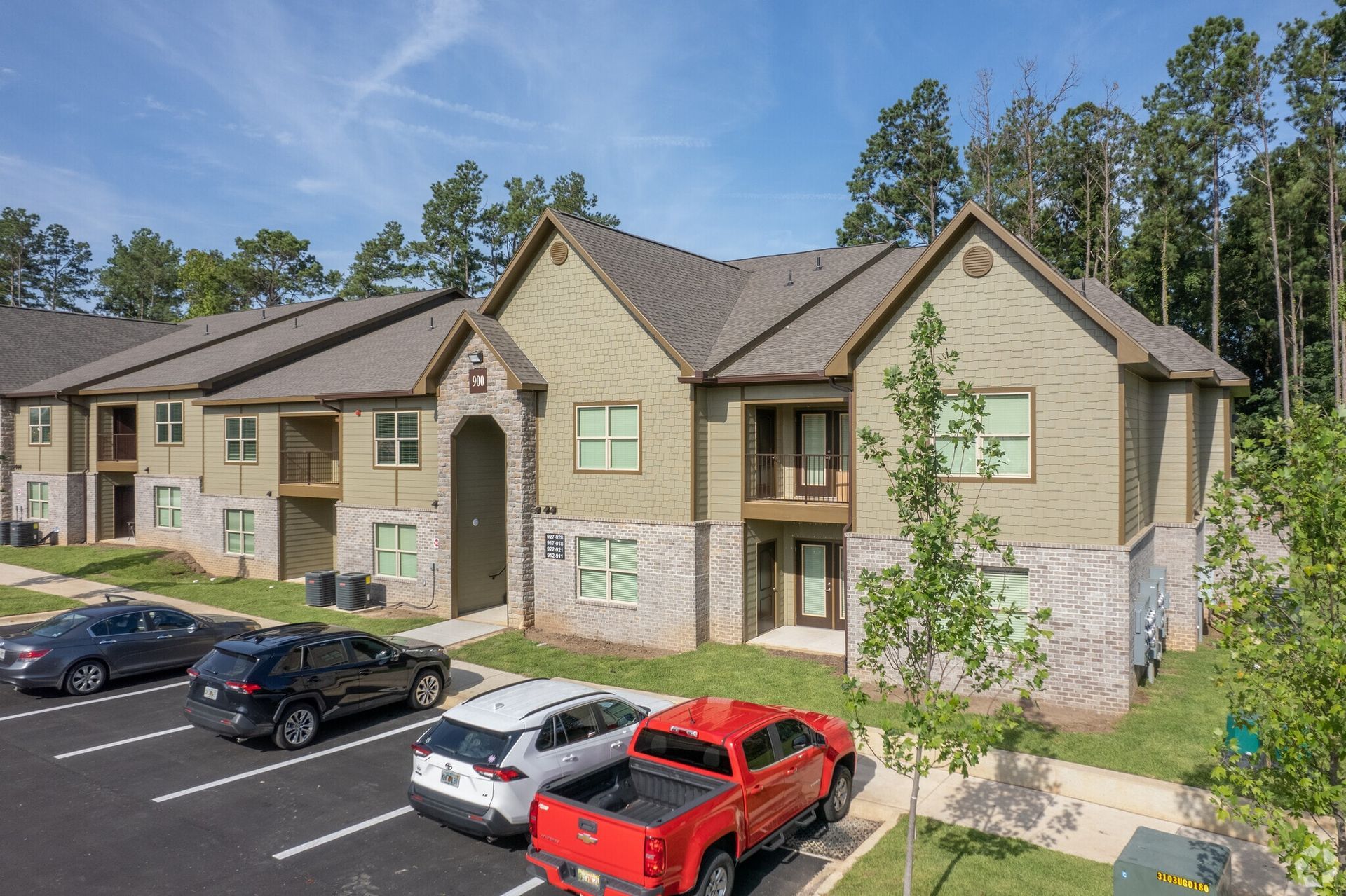 Exterior view of an apartment complex with parked cars and trees
