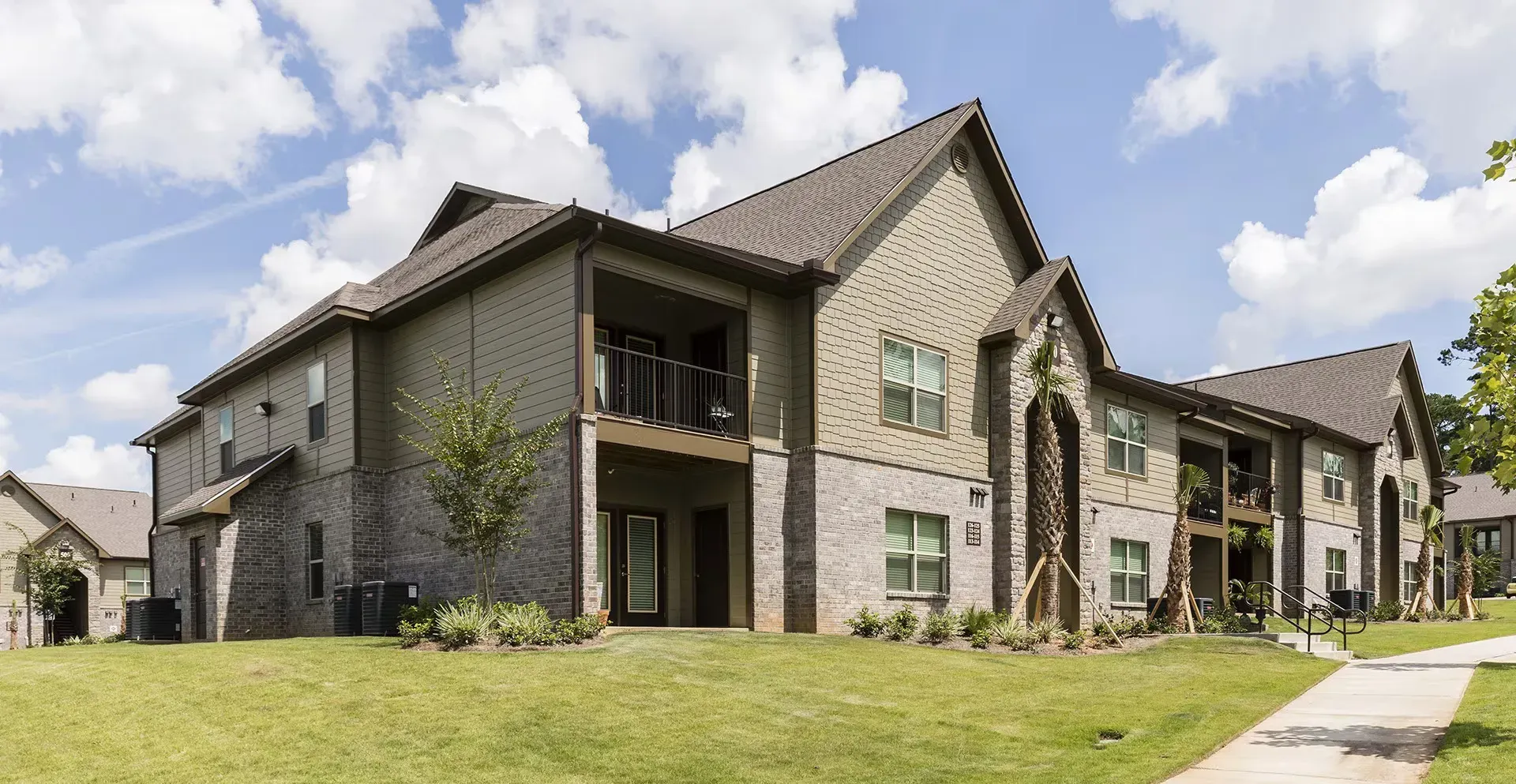 Exterior view of a modern apartment building with brick and siding, green lawn, and palm trees.