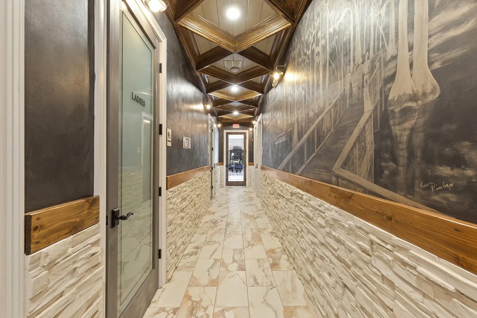 Interior corridor with a door labeled Ladies, stone wainscoting, and a mural on the right.