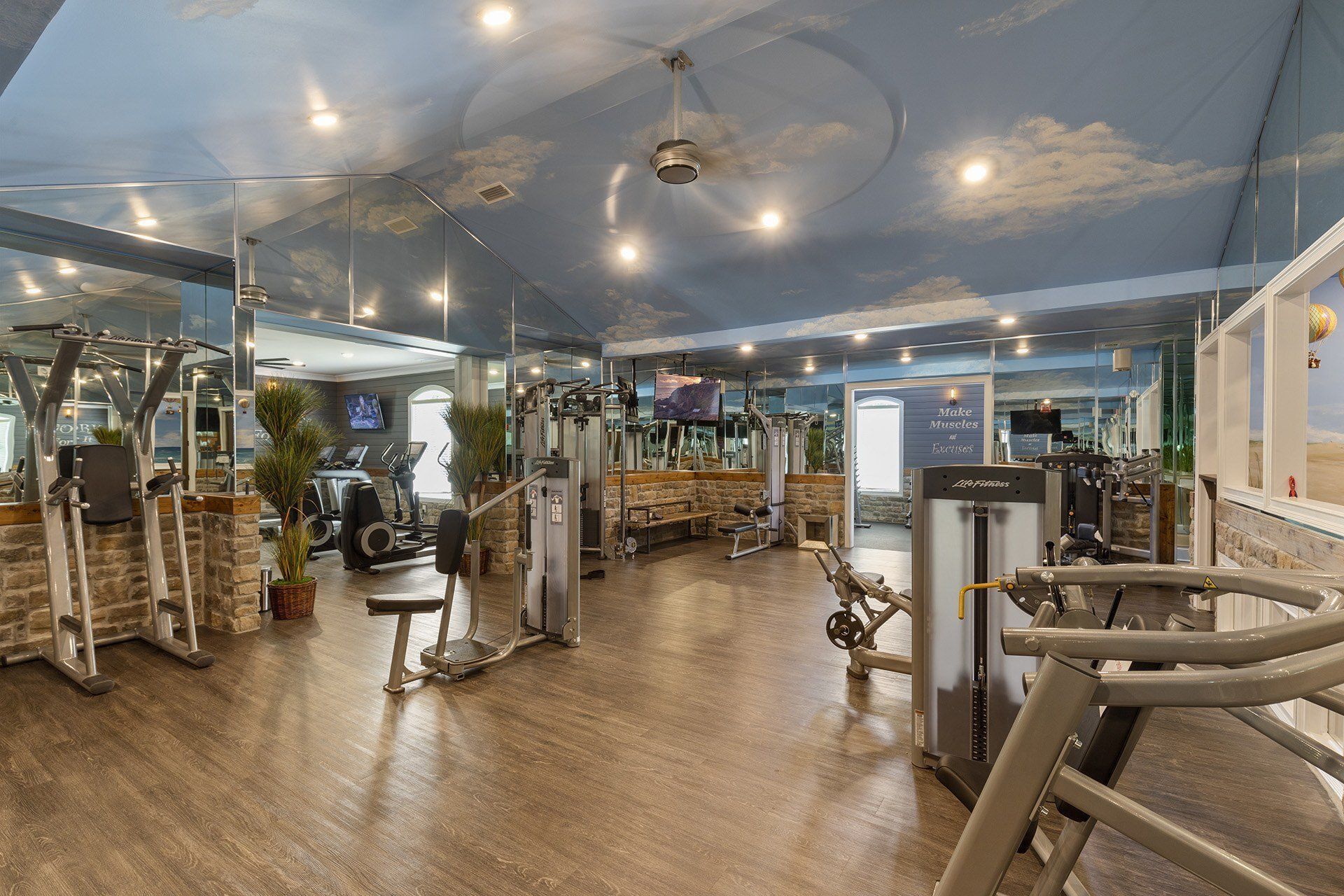 Indoor community gym with cardio and strength machines, mirrors, and wood-style flooring.