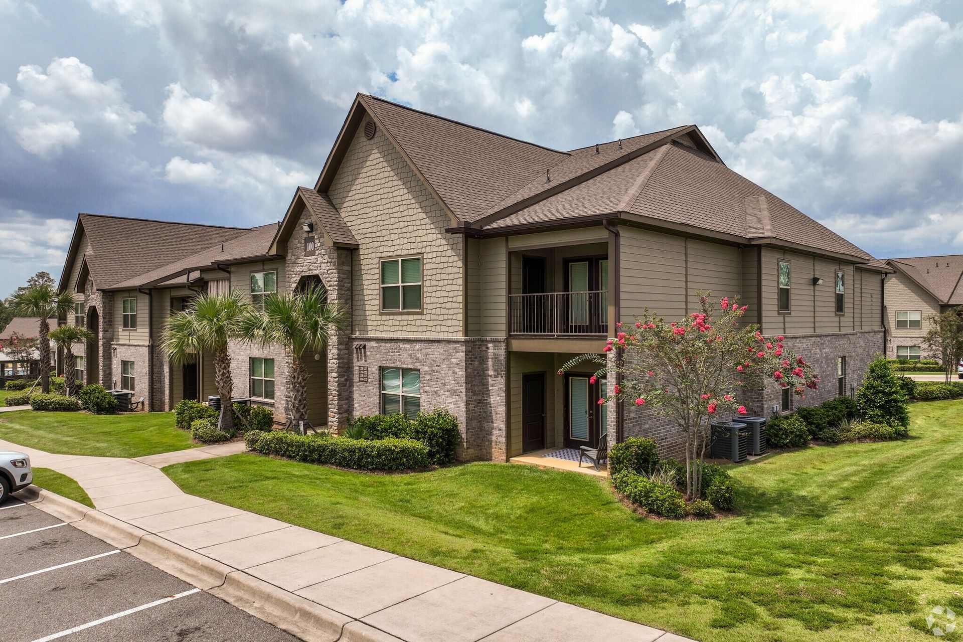 Exterior view of a multi-unit apartment building with brick and siding and manicured lawn.