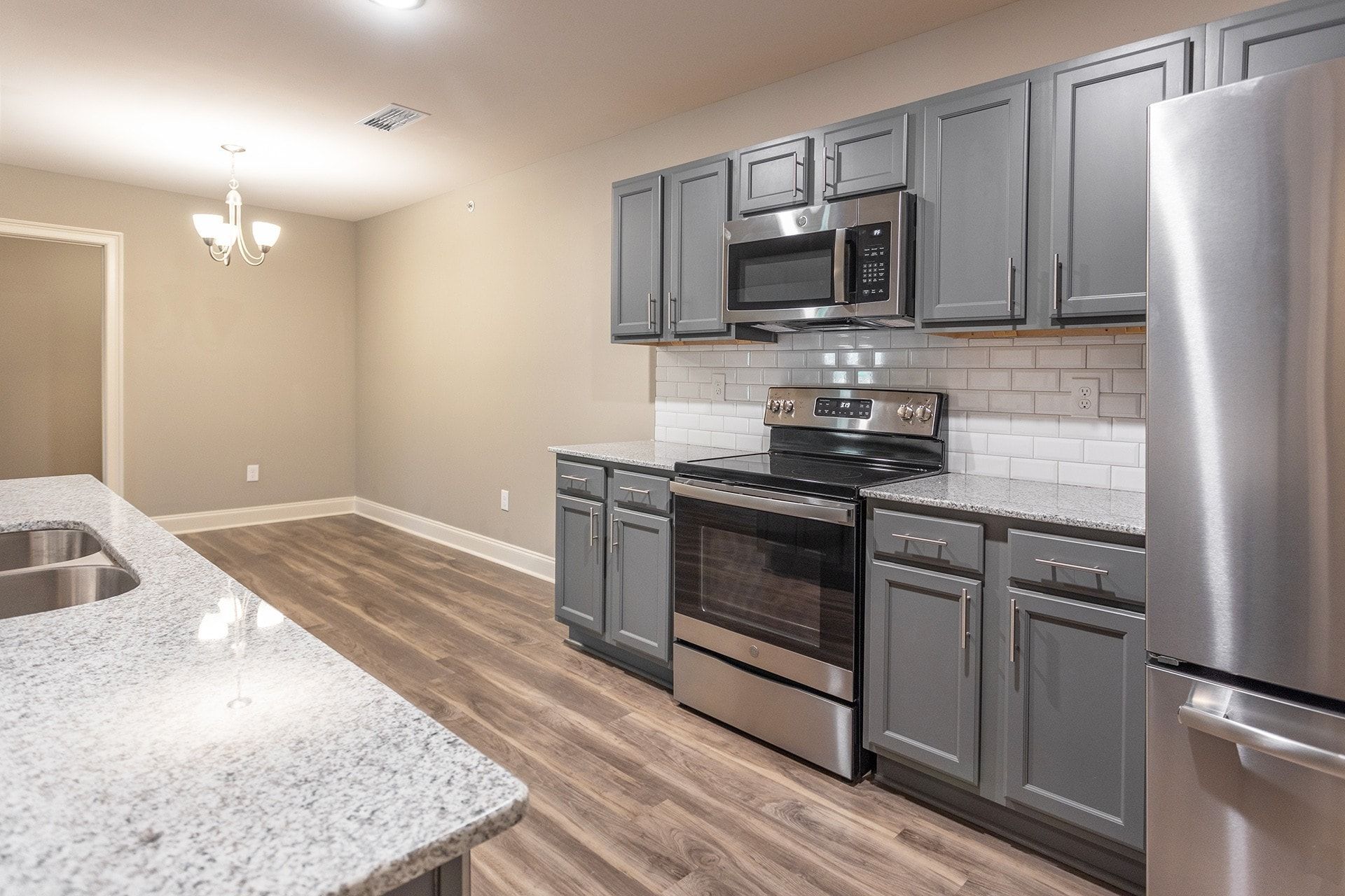 Modern apartment kitchen with gray cabinets, stainless steel appliances, and granite countertops.