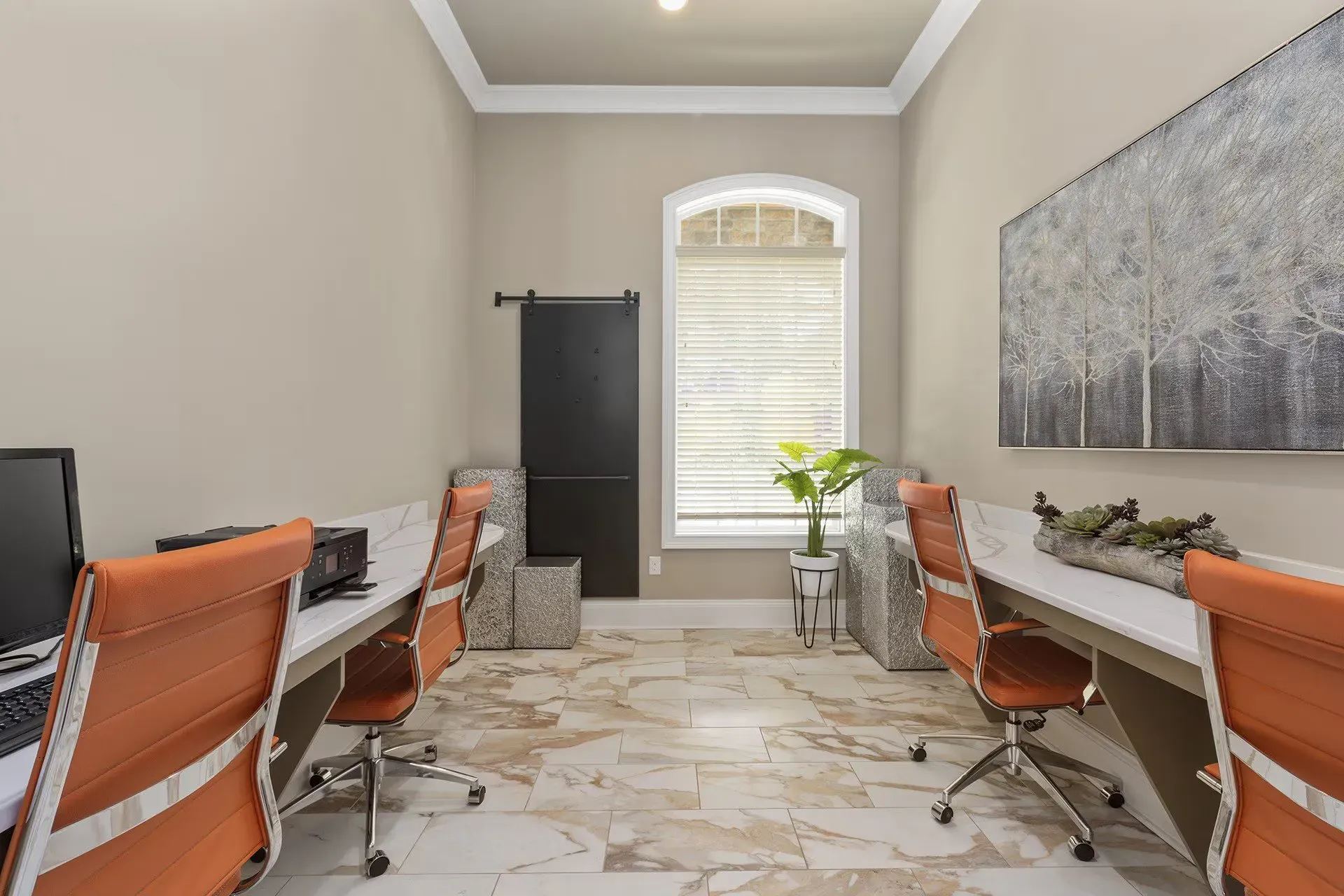 Shared leasing office with two desks, orange chairs, and a window in a neutral common space.
