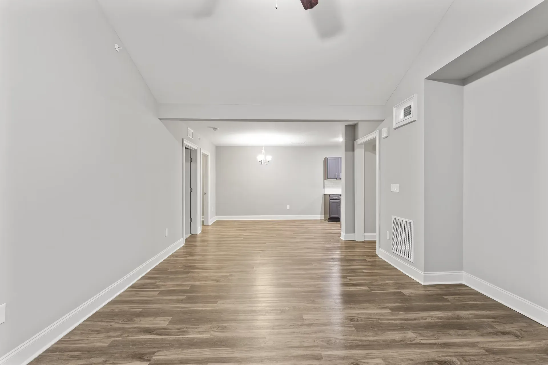 Open living area with gray walls, wood-look flooring, and a partial kitchen in the background.