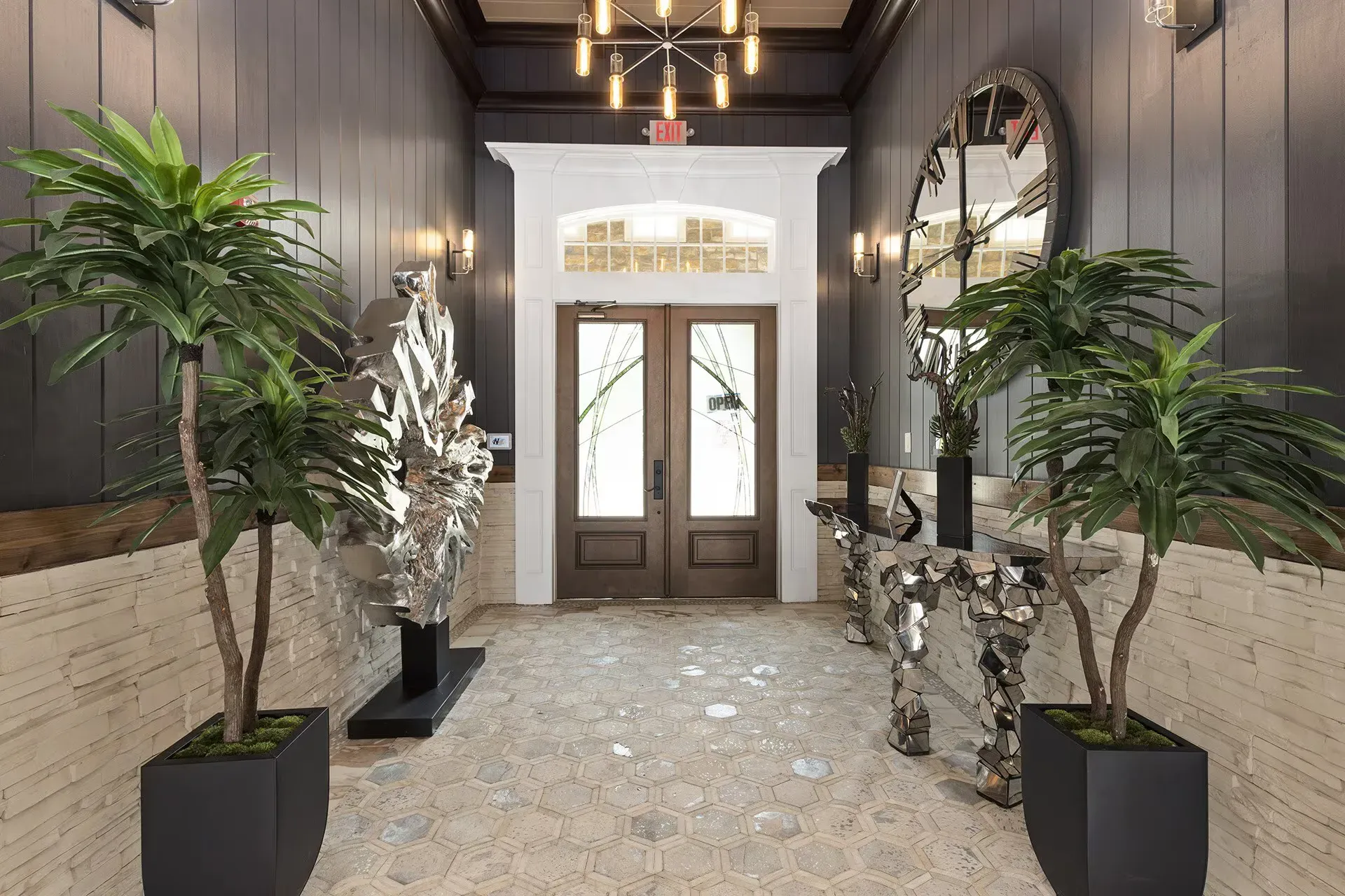 Entry lobby with double wooden doors, hex-tiled floor, plants, and a large round clock.