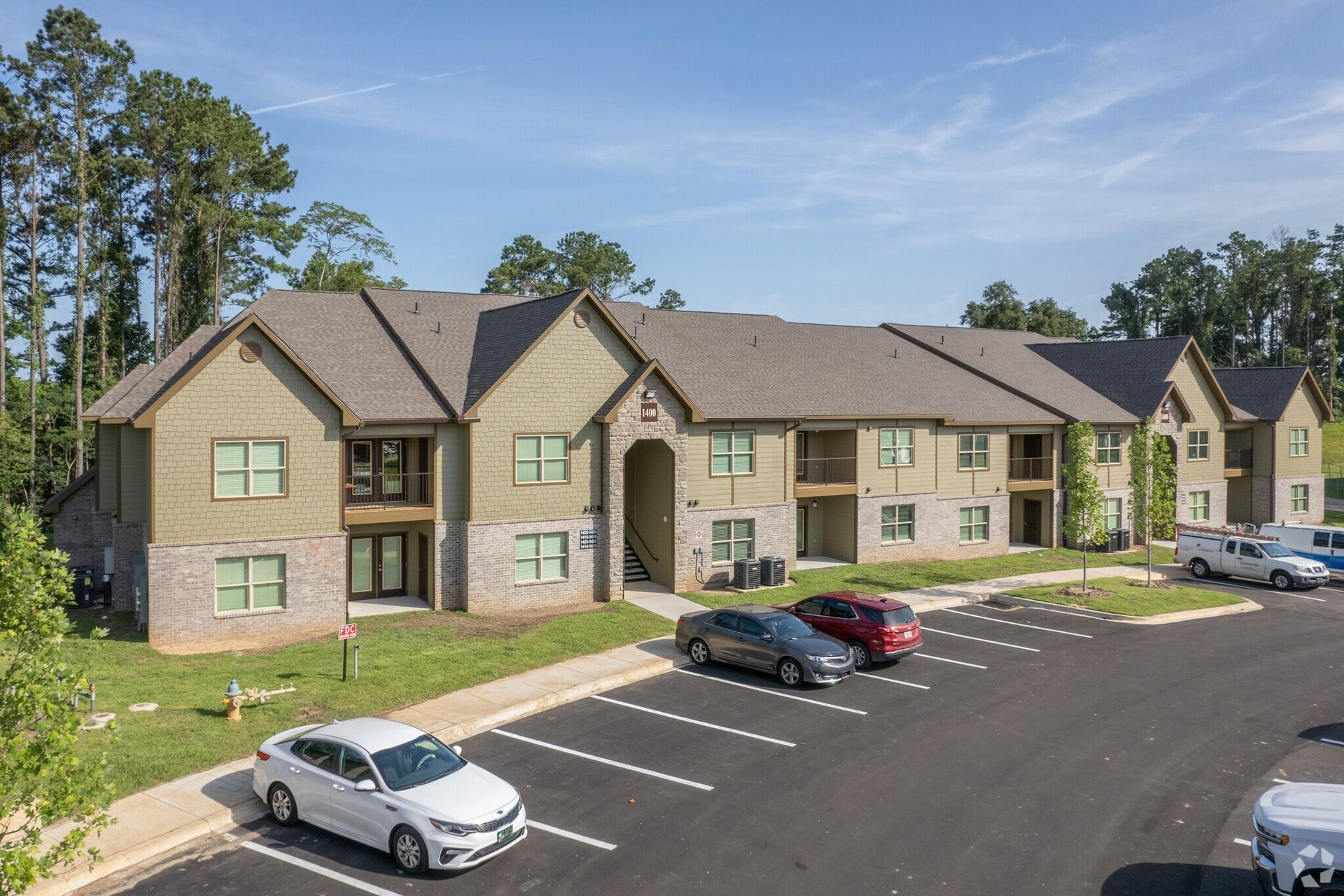 Aerial view of a beige multifamily apartment building complex with a parking lot and surrounding trees.