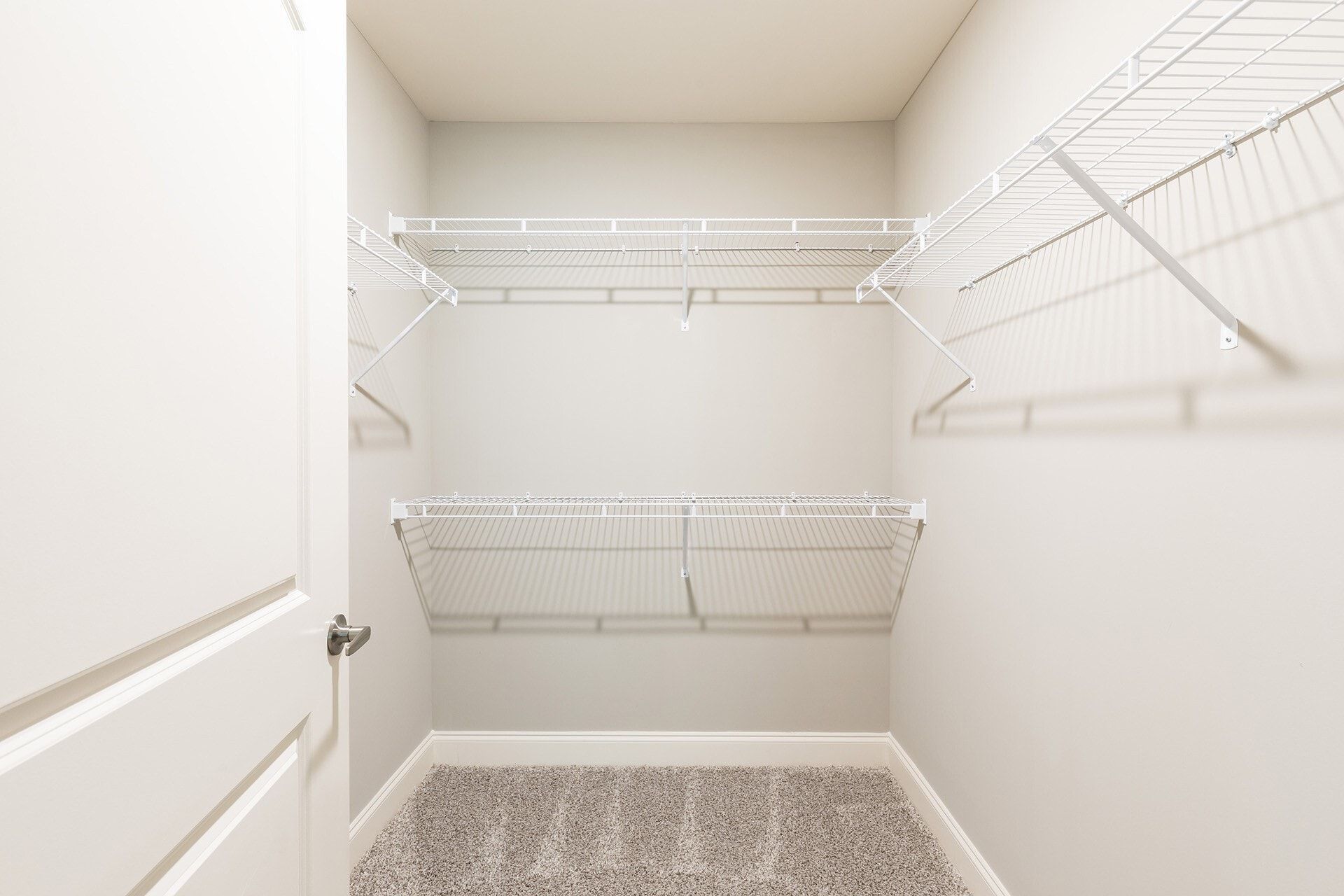 Empty walk-in closet with white wire shelving and beige walls.