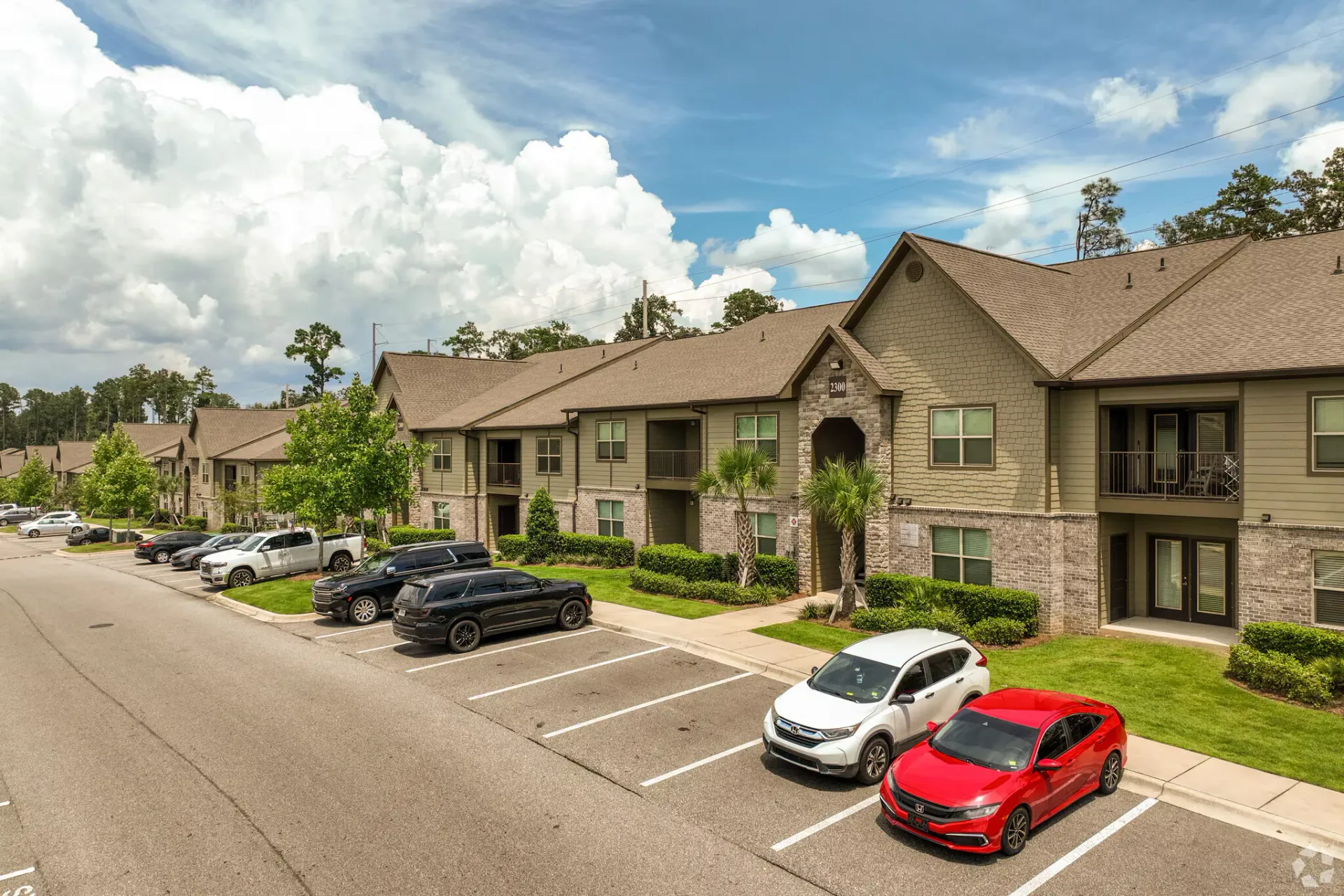 Exterior view of a multi-building apartment complex with a parking lot and green landscaping.