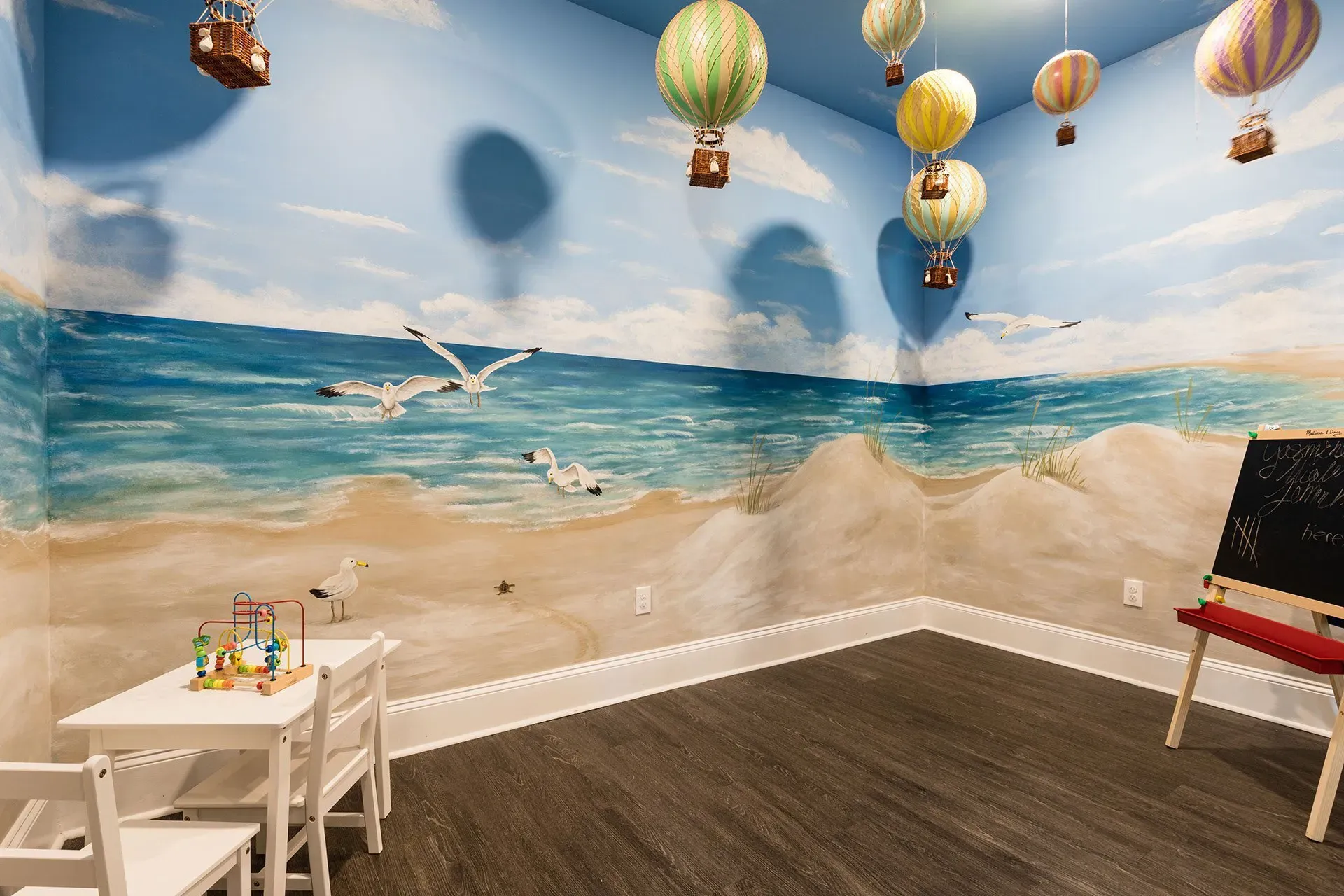 Kids’ playroom with a beach mural, seagulls, balloon decor, and a small white table with chairs.