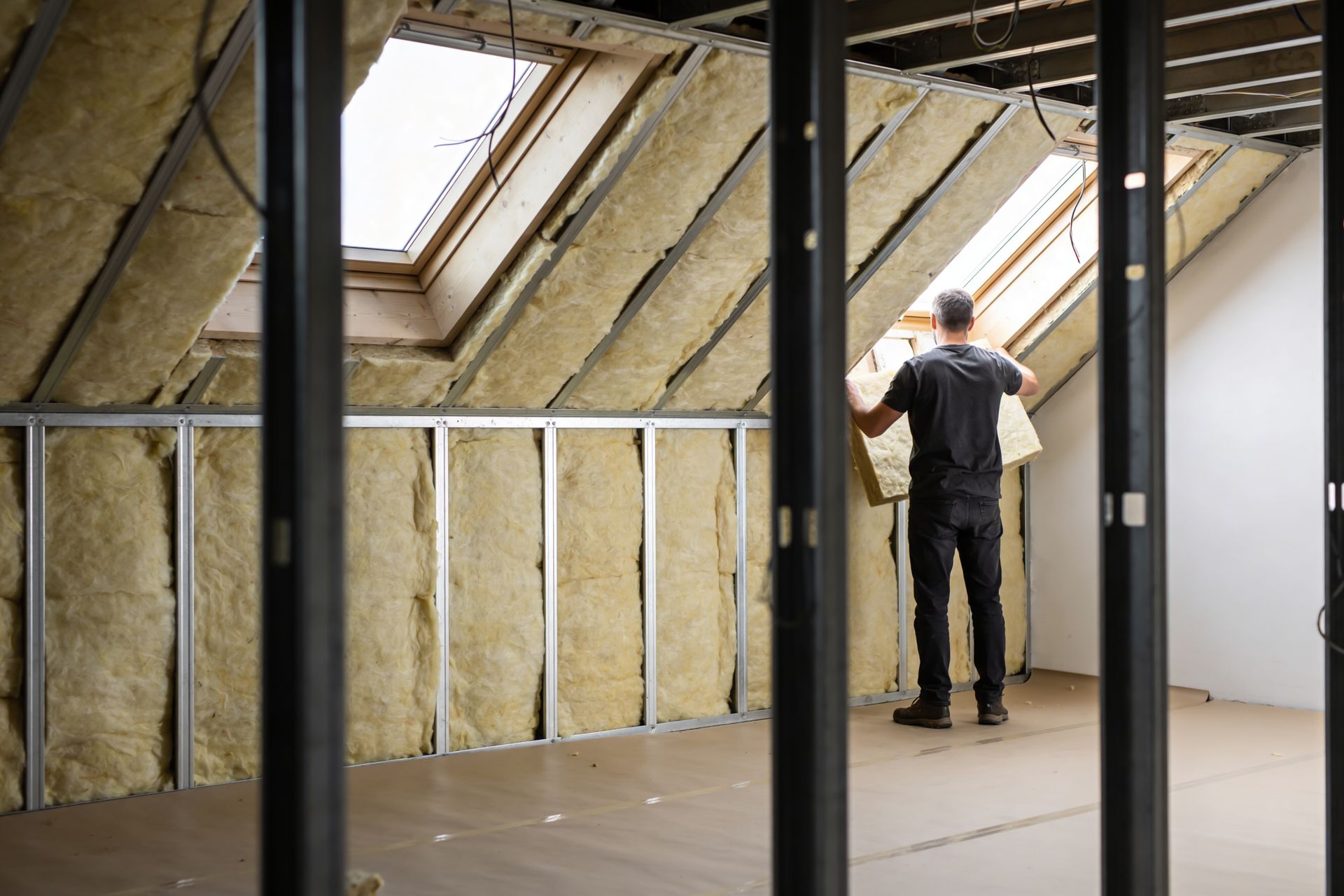 Person installing insulation in an unfinished attic with exposed framing and skylights