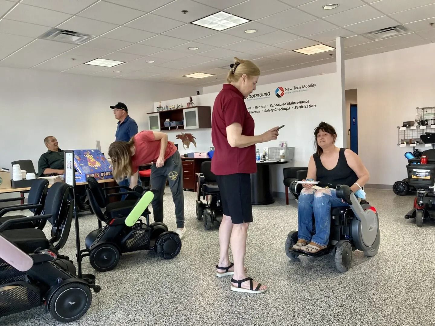 People in a showroom with mobility devices. A woman in a wheelchair talks to another woman; others observe.