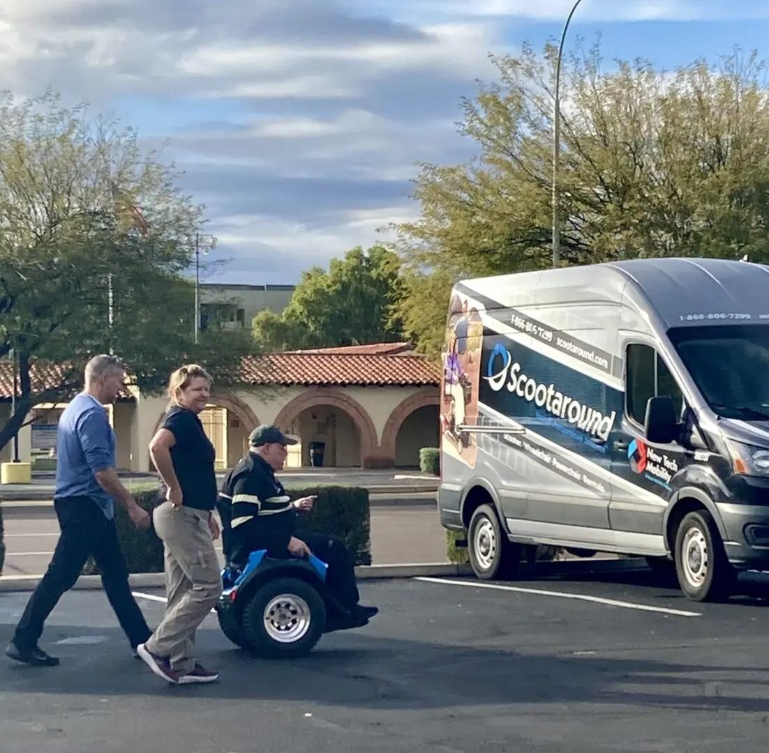 Two people walk with a person using a mobility scooter toward a Scooteround van in a parking lot.