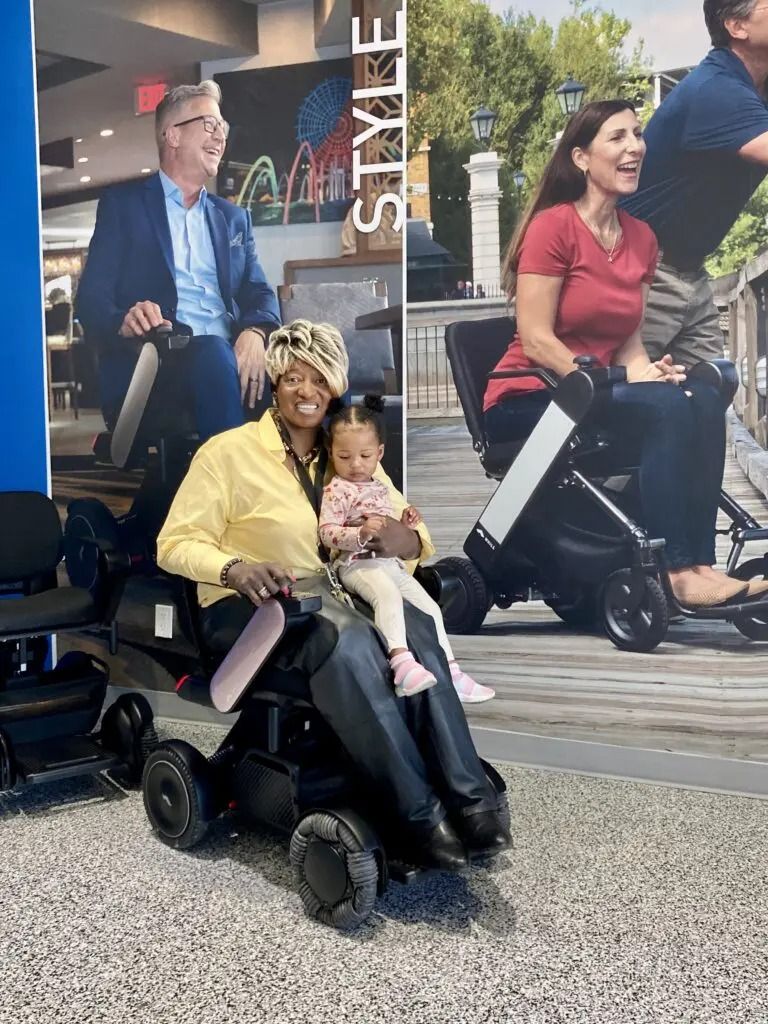 Woman and child sit on power wheelchair in front of display with people in wheelchairs.
