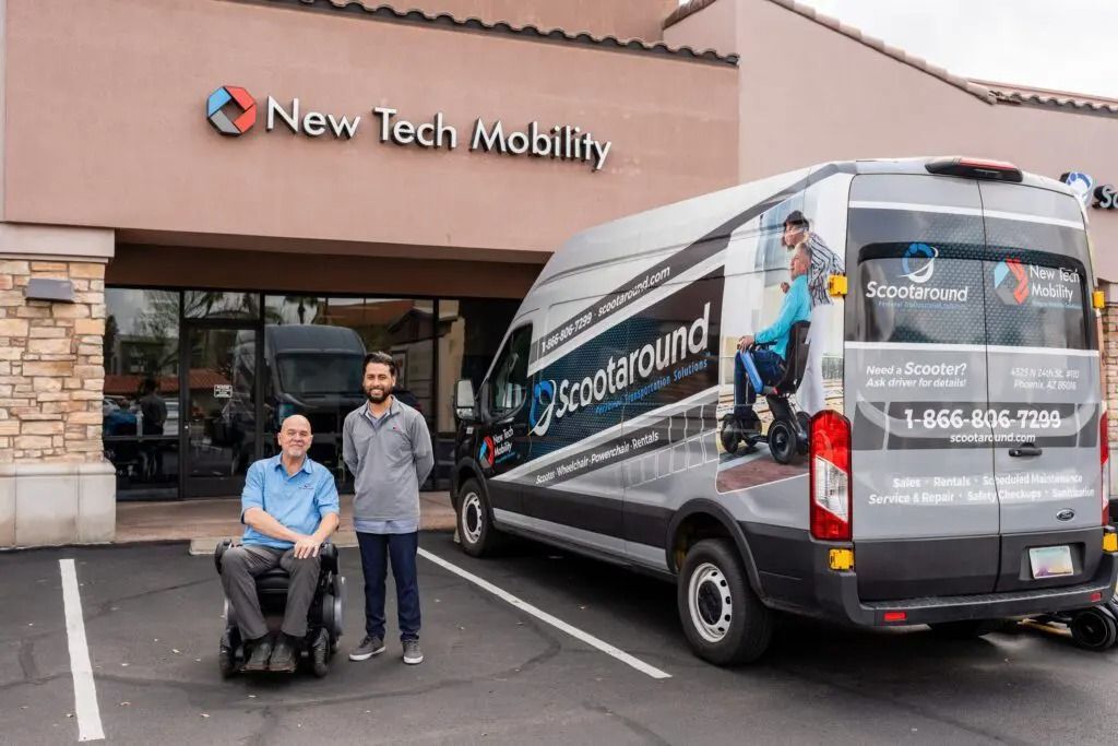 Two men by a Scootaround van and New Tech Mobility store. One man in a wheelchair, one standing.