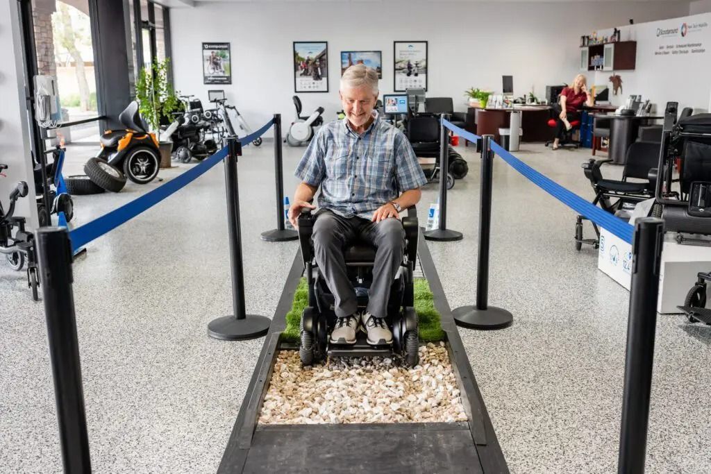 A man in a wheelchair tests mobility on an indoor obstacle course with rocks and artificial turf.