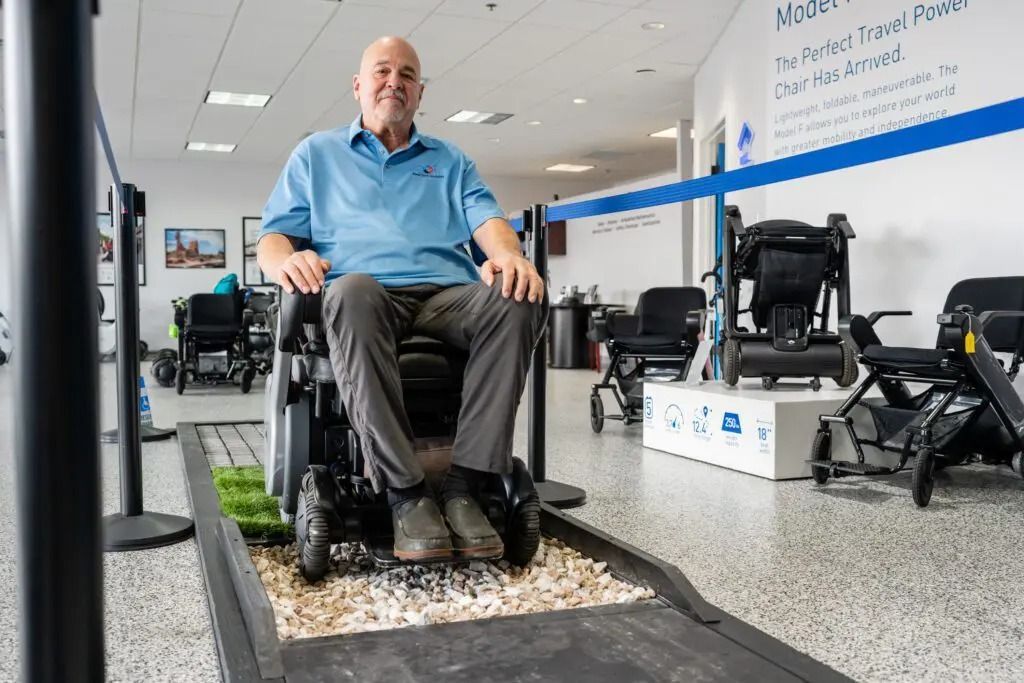 Man in wheelchair on a demo track. He's smiling in a showroom with mobility aids.