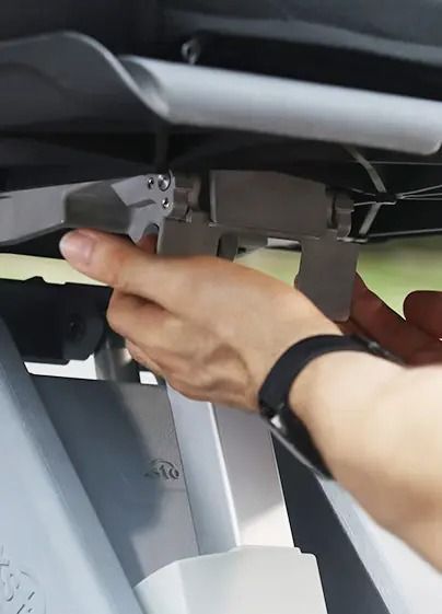 Person's hand adjusting a gray, hinged mechanism under a shelf.