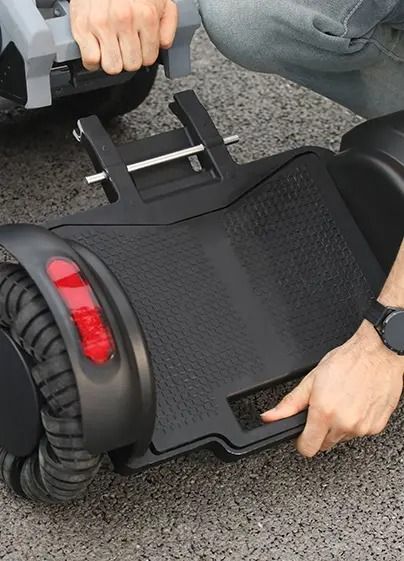 Person attaching a gray attachment to a black self-balancing scooter.