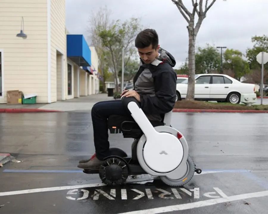 Man in a motorized wheelchair on a wet parking lot. The chair is white, silver, and black.