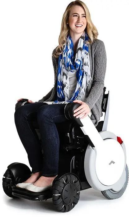 Woman smiling, seated in a black and gray folding mobility device.