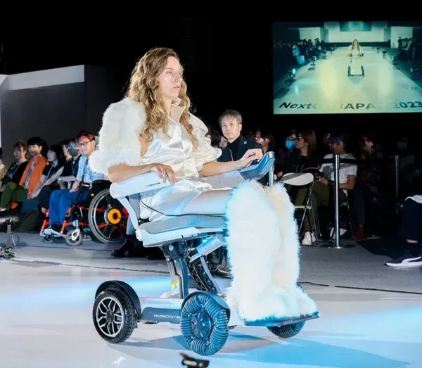 Woman in white outfit, wheelchair on fashion runway, showcasing adaptive fashion during a show.