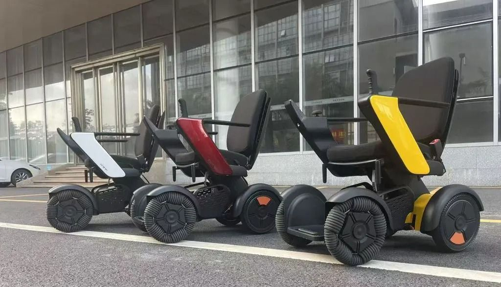 Three motorized, personal mobility devices in gray, red, and yellow, parked outdoors near a building.