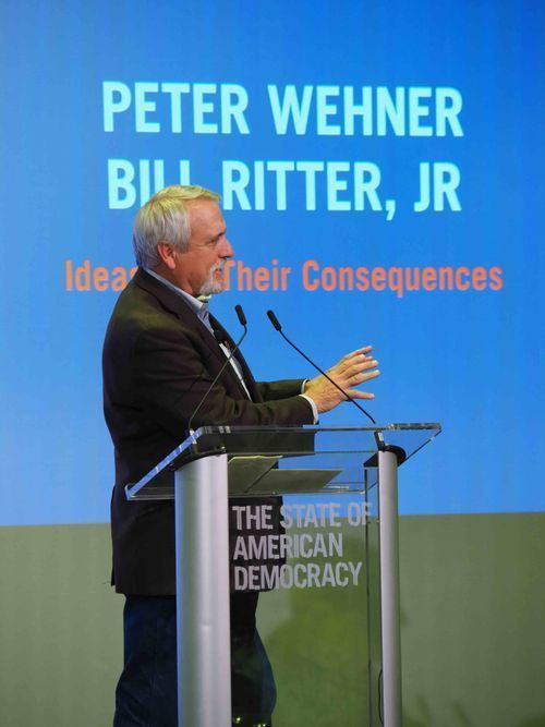 A man gestures while speaking at a podium labeled 